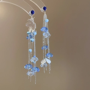 Detail of floral tassel earrings with white petals and blue beads on acrylic stand