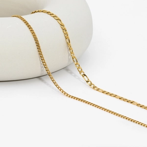 Detail of golden Figaro chain necklace on a white ring stand with polished metallic texture