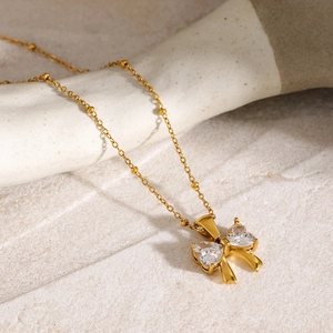 Detail of 18k gold plated bow necklace with heart-shaped white zircon stones on beaded chain