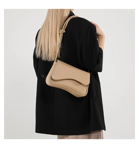 Model wearing a chic beige crossbody bag with a unique curved flap and knotted strap detail