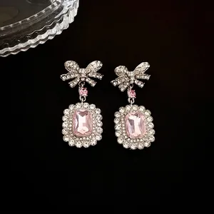 Boucles d'oreilles nœud en argent avec cristaux roses rectangulaires sur fond sombre