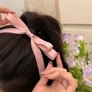 Pink satin double bow hair clip with long ribbons worn on wavy brunette hair