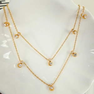 Elegant gold double-layer necklace with round cubic zirconia drops on a ceramic display