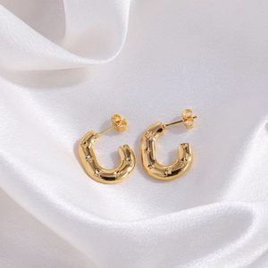 Detailed view of gold U-shaped earrings with embossed stars on white silk fabric