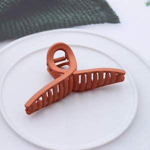 Detail view of large orange matte hair claw clip with crossed design on a white plate