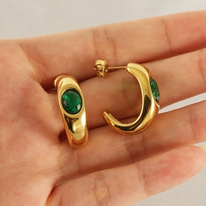 Macro view of gold C-shaped earrings featuring a central oval green gemstone inlay