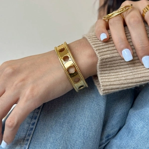 Detail of a gold wide hollow cutout cuff bracelet worn on a woman's wrist