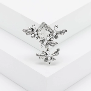Silver dragonfly brooch with white pearls displayed on a white geometric platform