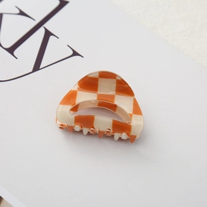 Detail shot of mini checkerboard hair claw clip in orange and beige acetate finish