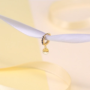 Detail of a gold hoop earring with blue gems and polished gold ball on a ribbon
