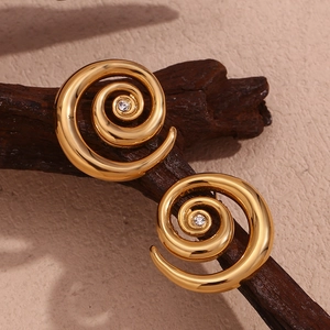 Macro detail of gold-plated spiral earrings with zircon stone on textured wood background