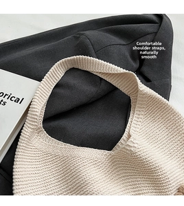 Detail of cream knit shoulder bag showing wide strap texture on a grey blazer