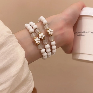 Close-up of white acrylic beaded bracelet with a gold-edged flower charm on a model's wrist