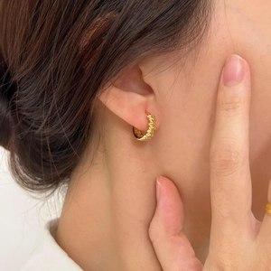 Close-up of a model wearing a gold croissant hoop earring with a polished twisted texture