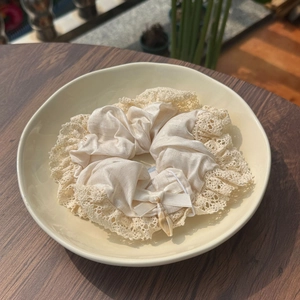 Close-up of cream lace scrunchie with silk texture and natural shell charm detail