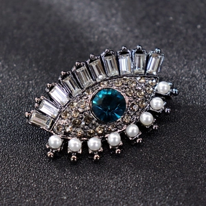 Detailed macro view of eye-shaped silver brooch with blue stone, pearls and white crystals