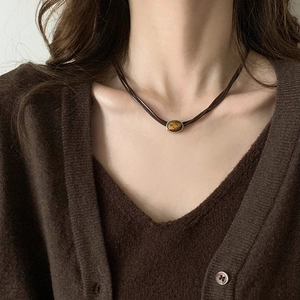 Close-up of model wearing oval tiger eye stone necklace with brown cord on collarbone