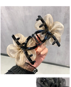 Detail of elegant gold flower hair claw clip with pearls held by hand against grey wall