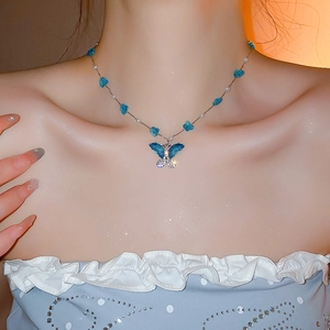 Vista detallada de un collar de mariposa azul con perlas en la clavícula de una modelo