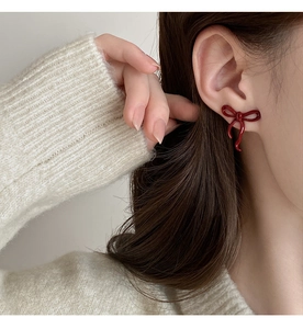 Close-up of a glossy red bow earring worn by a model in a cozy, elegant setting