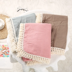 Detailed view of folded cotton muslin baby blankets with soft fringe trim in three colors