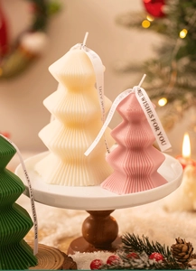 Three colorful origami Christmas tree scented candles on a white stand with holiday decor