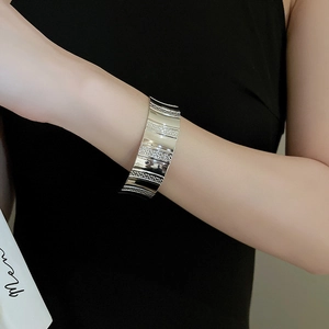 Close-up of wide silver metallic open cuff bracelet with alternating textured stripes
