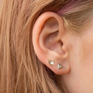 Detailed close-up of golden geometric triangle and rhombus stud earrings on a model