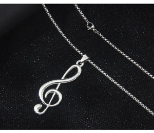 Close-up of a silver treble clef musical note necklace on a black textured background