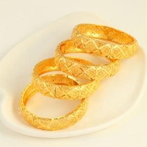Close-up of four gold-plated hollow bangles with intricate floral patterns and clasp details