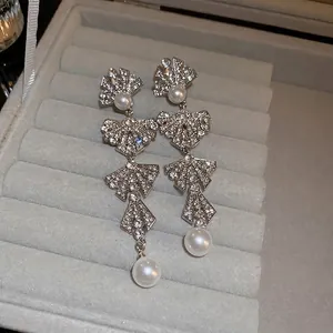Elegant silver bowknot earrings with cascading pearls and rhinestones on a velvet surface