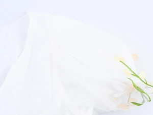 Détail d'une robe en mesh blanc avec broderie de fleurs jaunes et vertes et manche plissée