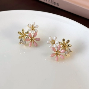 Macro shot of gold-plated daisy flower earrings with white pink enamel and zircon