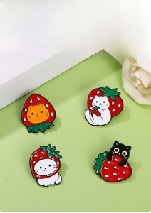 Detailed view of four cute enamel cat and strawberry pins on a soft green background