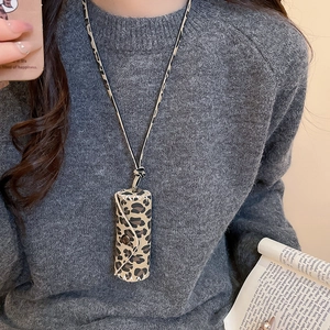 Close-up of leopard print leather pouch necklace with button closure and stitching detail
