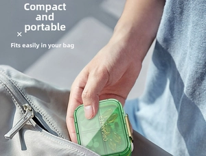 Green portable pill organizer with golden latch being placed into a pocket