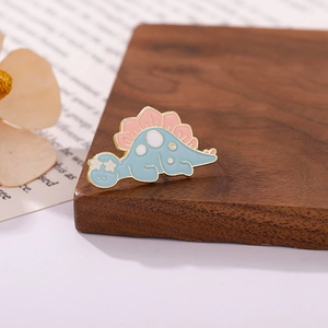 Detailed view of a cute pink and blue enamel dinosaur pin on a rustic wooden base