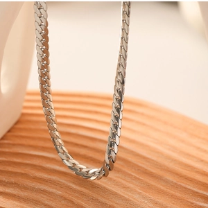 Close-up of a silver stainless steel snake chain necklace on a rustic wooden tray