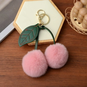 Detail of pink faux fur cherry keychain with green leather leaves and gold metal ring