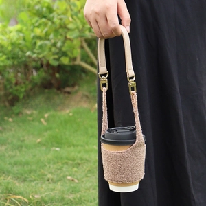 Brown fleece coffee cup sleeve with leather handle shown held over a green lawn background