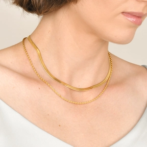 Detail of layered gold snake and twisted chain necklaces worn by a model