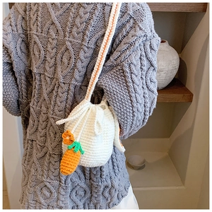 Detail of hand-woven rabbit bucket bag with orange carrot charms on a grey knit sweater
