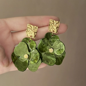 Macro detail of dark green acrylic flower earrings with golden textured metal accents
