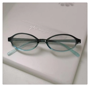 Detail view of oval teal gradient eyeglasses frame placed on a white notebook surface