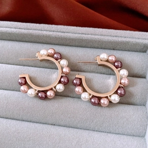 Close-up of C-shaped gold earrings with white, champagne, and purple pearls in a velvet box