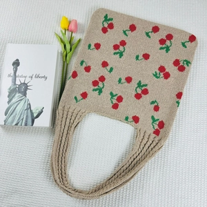 Close-up of khaki knitted tote bag with red cherry patterns and decorative tulips