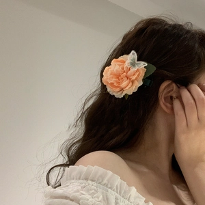 Detail of peach fabric flower hair claw with embroidered butterfly and green leaf accents