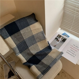Classic blue plaid oversized scarf with fringes draped on a chair in soft natural light