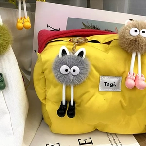 Close-up of bright yellow puffer bag with cute grey plush monster pendant and Tagi label