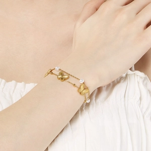 Detail of layered gold butterfly bracelet with white pearls shown on female wrist